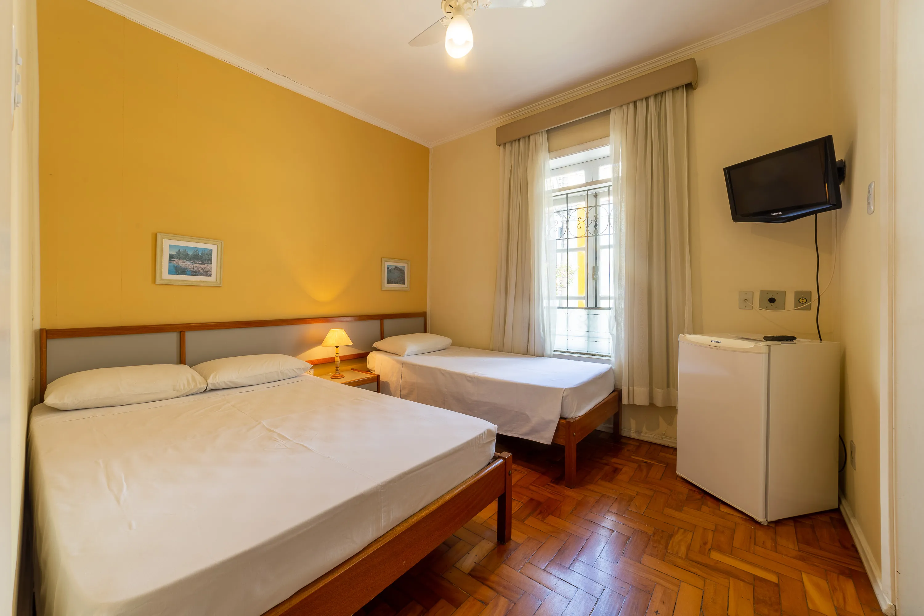 foto de quarto com ventilador, com uma cama de casal e uma cama de solteiro, capaz de acomodar até três pessoas, com tv, frigobar e banheiro