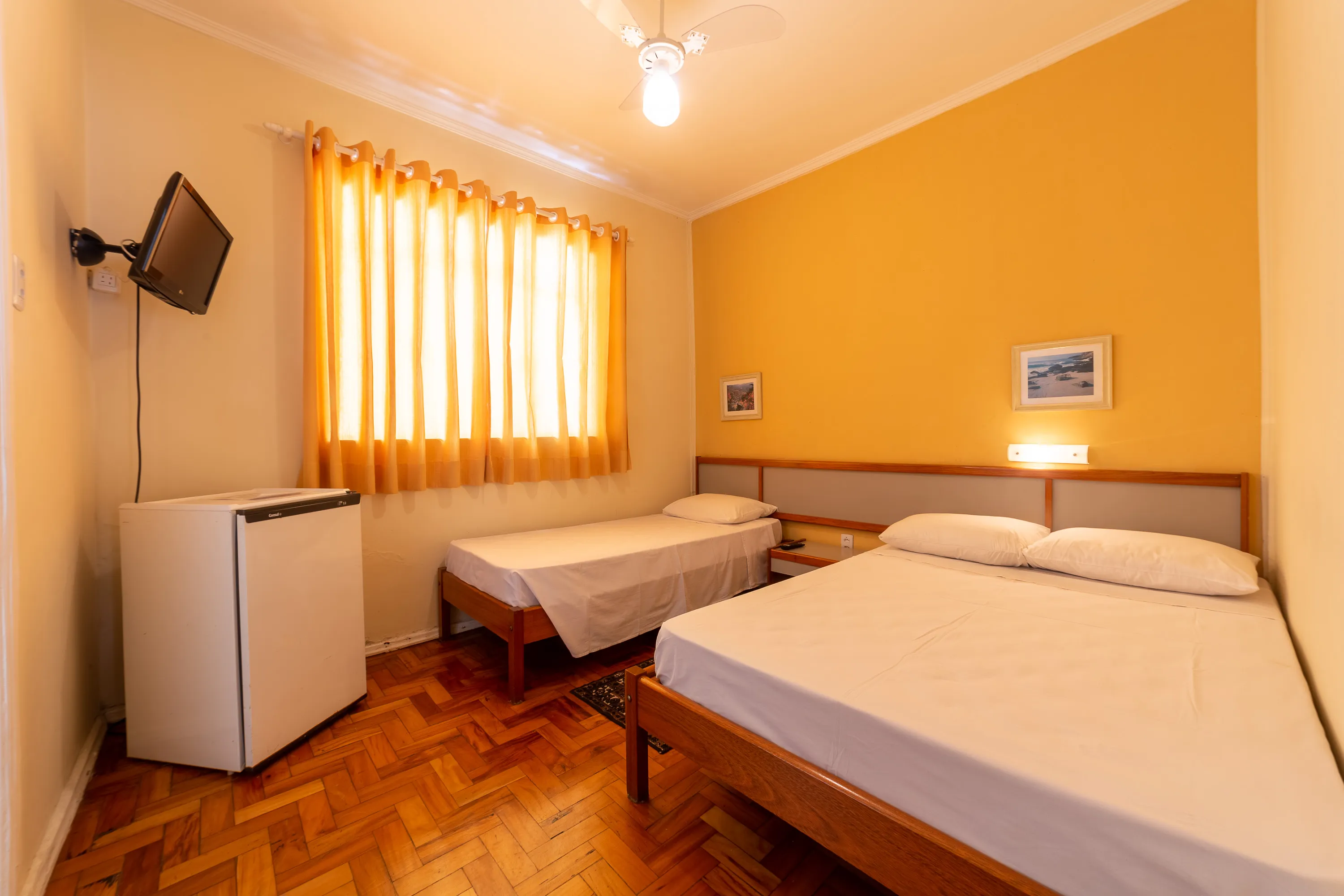 foto de quarto com ventilador capaz de acomodar até três pessoas, com uma cama de casal e outra de solteiro, equipado com tv, frigobar e banheiro privativo