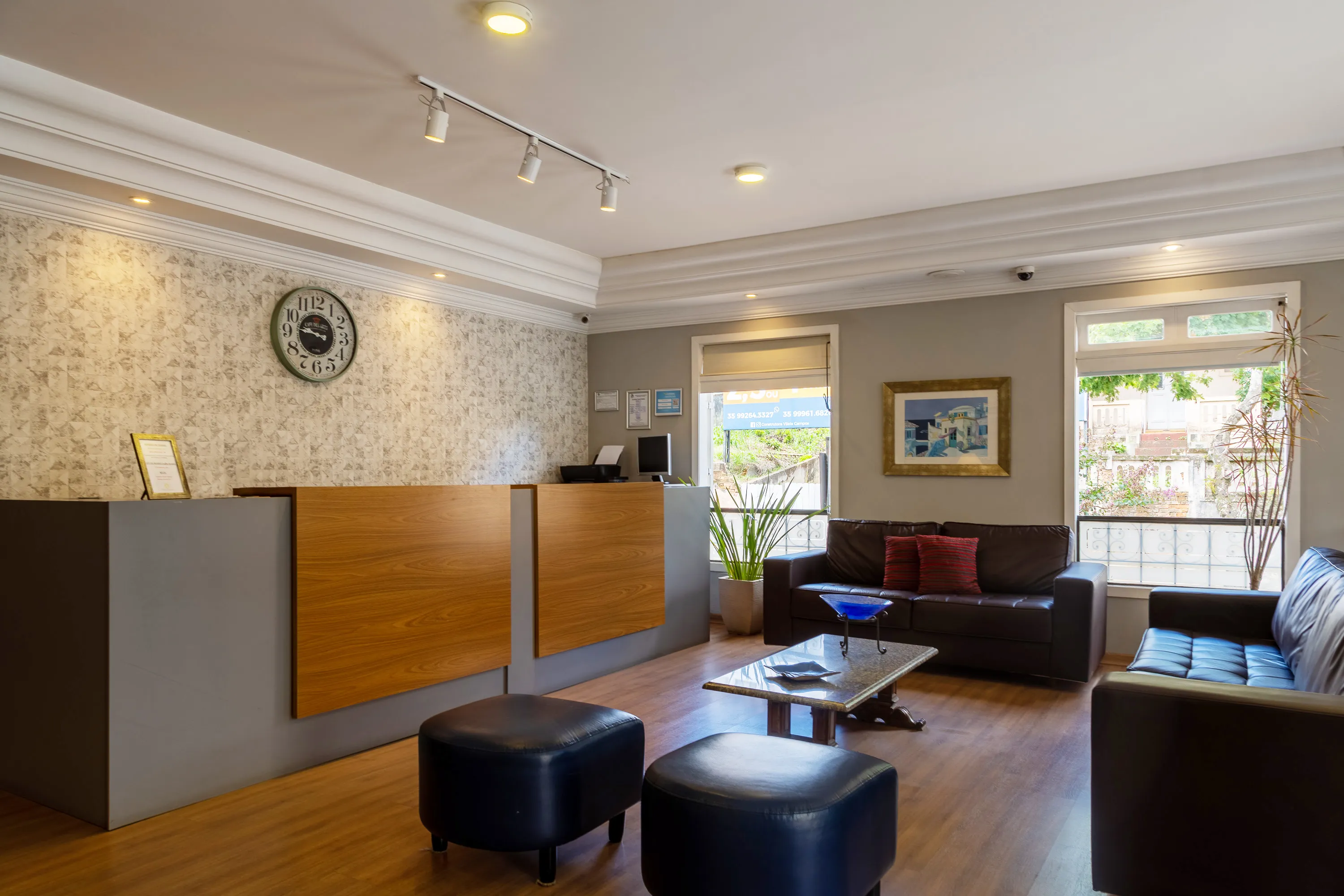 recepção do hotel com balcão e chão de madeira equipado com dois sofás grandes de couro marrrom paredes brancas e sanca de gesso bem detalhada no teto
